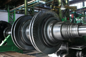 Large industrial turbine components displayed in a factory setting with machinery and overhead beams in the background.