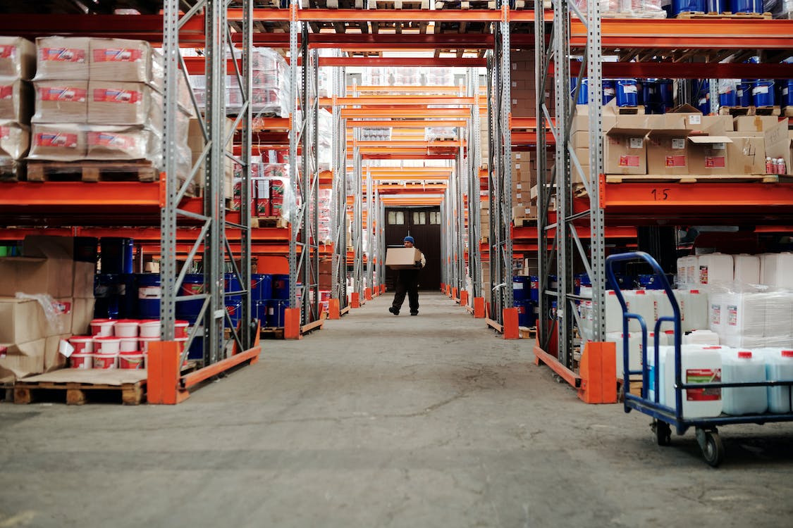 Warehouse logistics, worker in uniform carrying box in industrial storage room, supply chain management